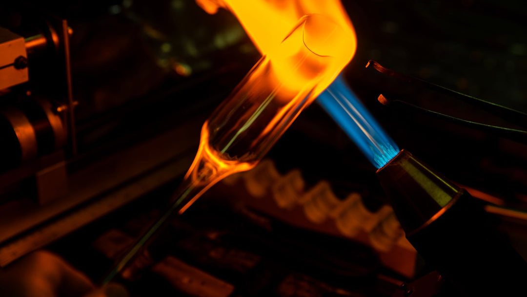 A glass tube glowing orange as it softens in the blue jet flame of a bench torch, dark workshop background