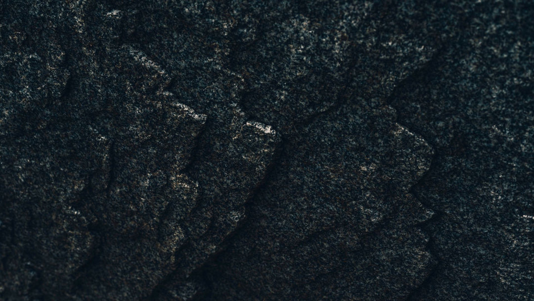 A close view of a dark speckled granite face broken into stepped angular ledges, with pale mineral flecks catching the light along the edges