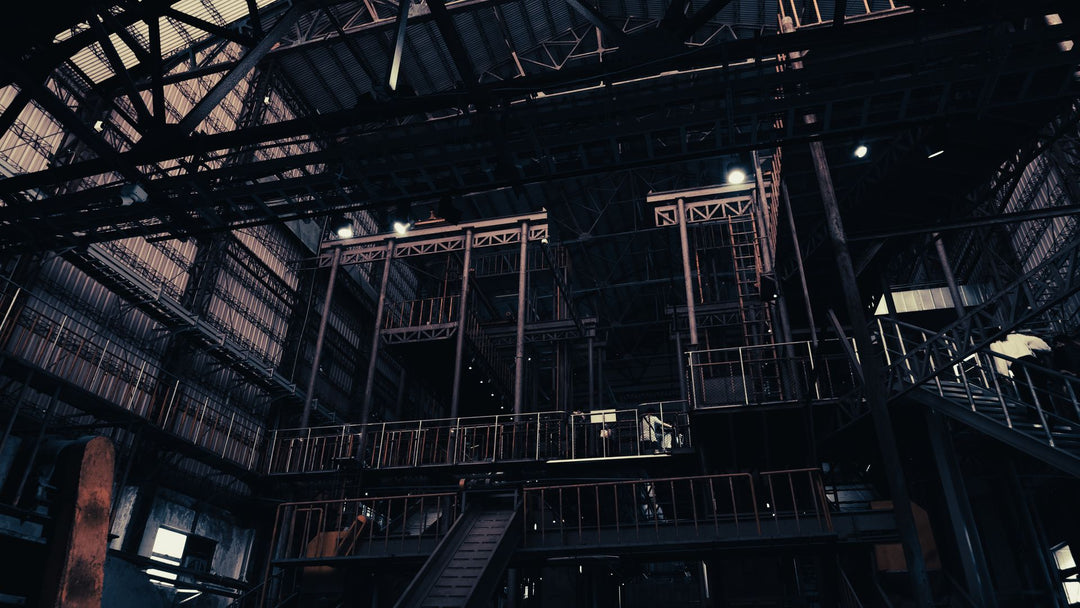 Looking up inside a dark industrial steel-frame building with catwalks, girders and overhead lighting
