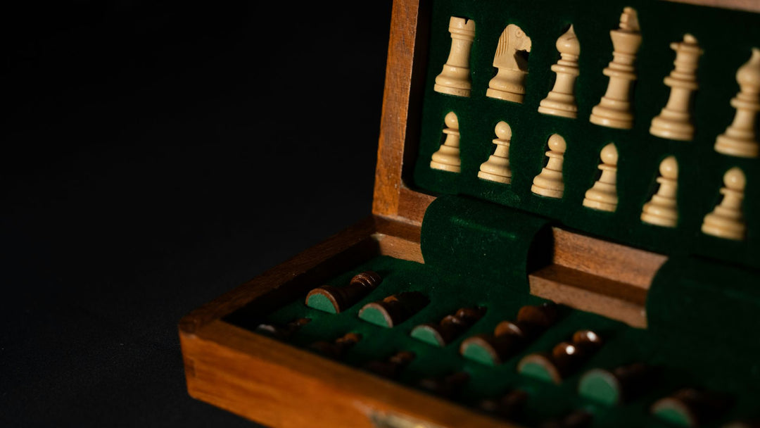 An open wooden box with a chess set inside, ivory and dark wooden pieces nested in green felt, dark background