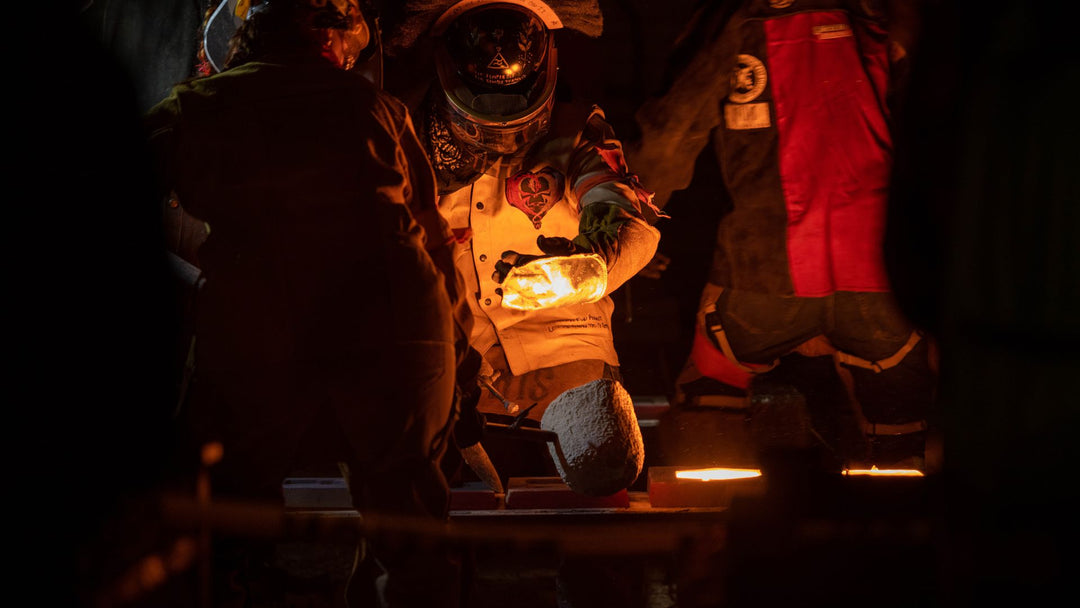 A foundry worker in full protective gear handling glowing molten metal in a dark industrial setting