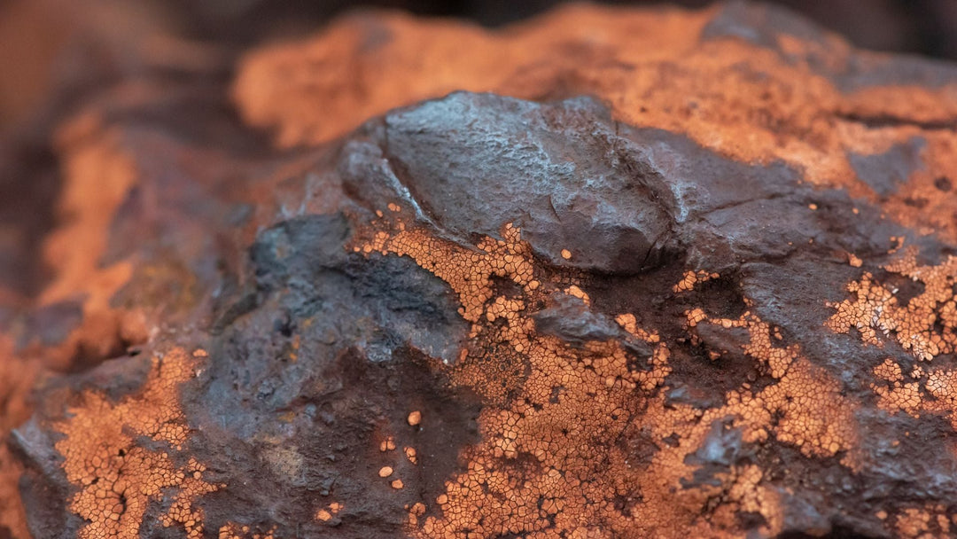 Close-up of a rusted iron ore mass, dark blue-gray metal showing through a cracked orange oxide crust