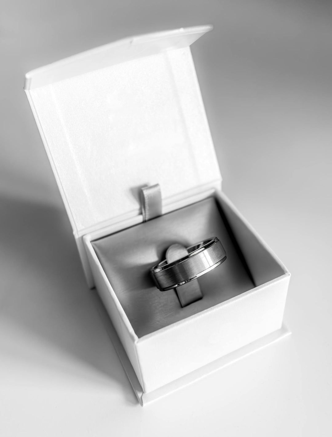 Wide brushed silver tungsten wedding band in an open white ring box