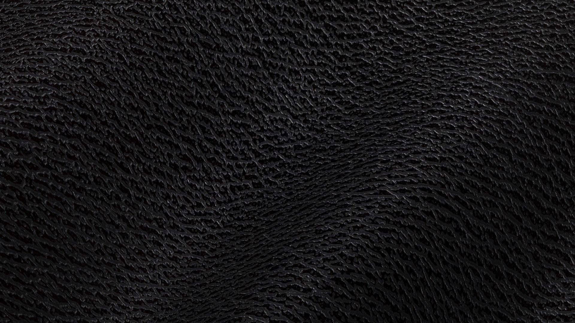 Close-up of dark pebbled black leather falling in soft folds, lit low from one side