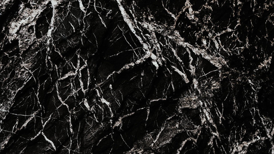 Close-up of black marble stone with dense white mineral veining in a dark, moody texture