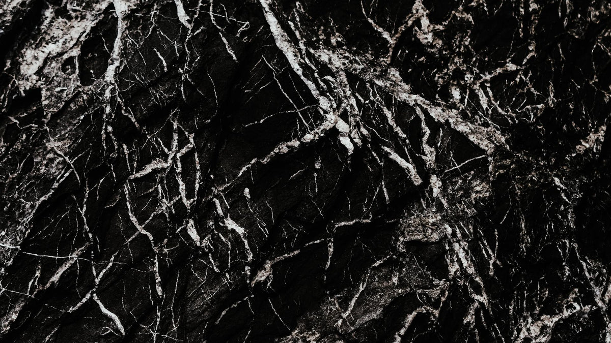Close-up of black marble stone with dense white mineral veining in a dark, moody texture