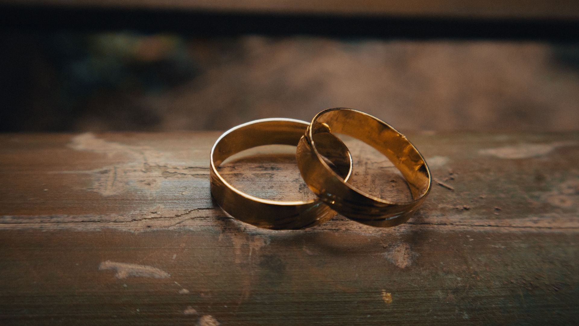 Two interlocking gold wedding bands on rustic wood under warm, dramatic lighting