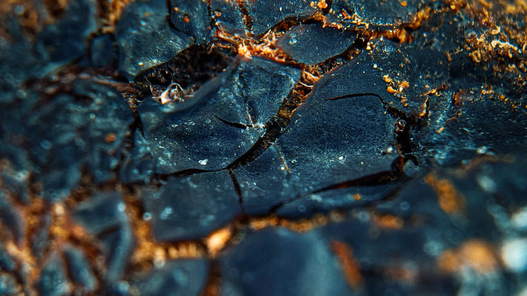 Macro view of a dark blue-grey mineral surface broken into angular plates, with rust-orange veins running through the cracks between them