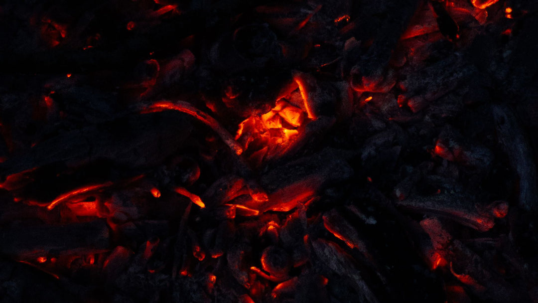An overhead bed of black charcoal glowing with red and orange embers, a bright ignition point above center