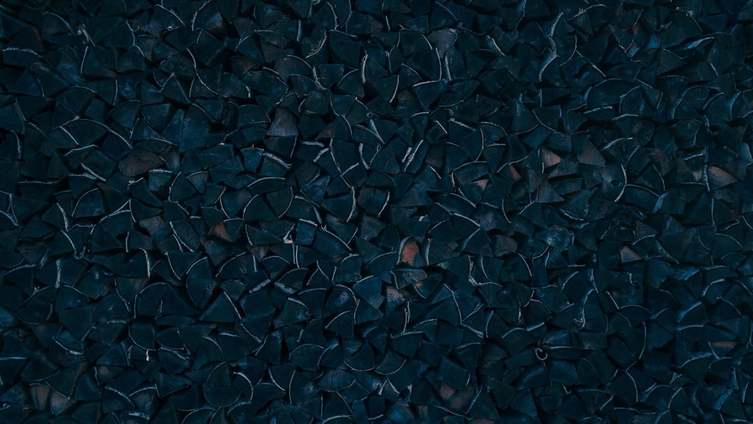 Dark navy-toned stacked firewood ends, cut and split, filling the frame
