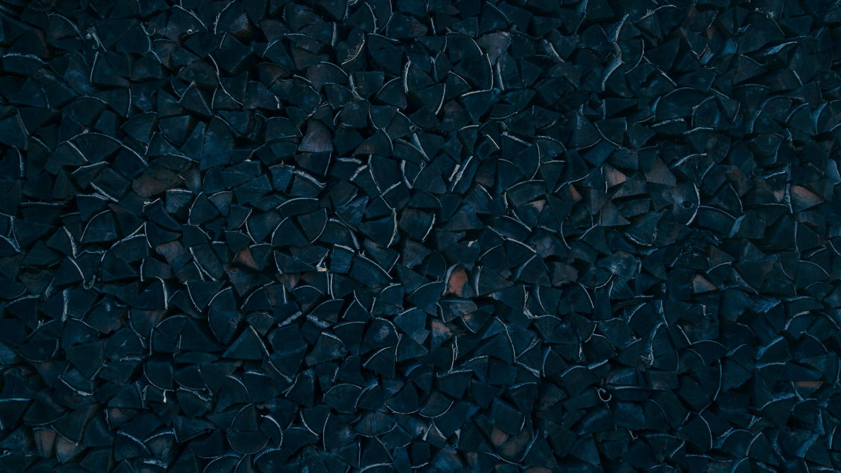 Dark navy-toned stacked firewood ends, cut and split, filling the frame