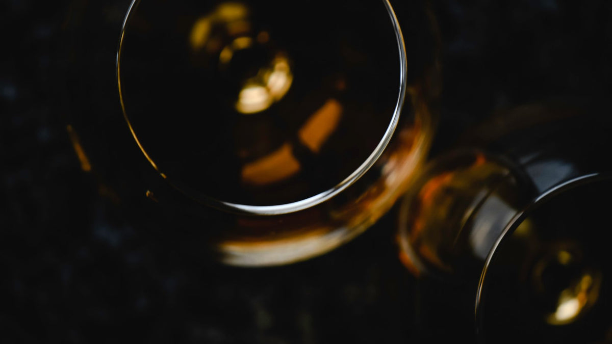 two glasses of amber whiskey photographed from above on a dark table