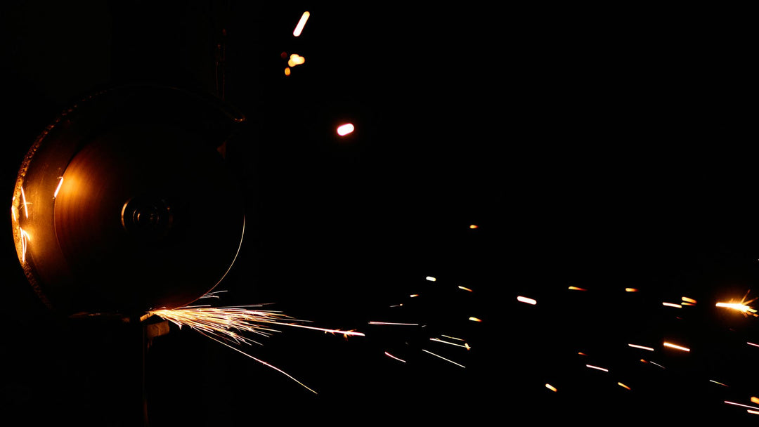 An abrasive cutting wheel throwing a fan of gold sparks across a black workshop background