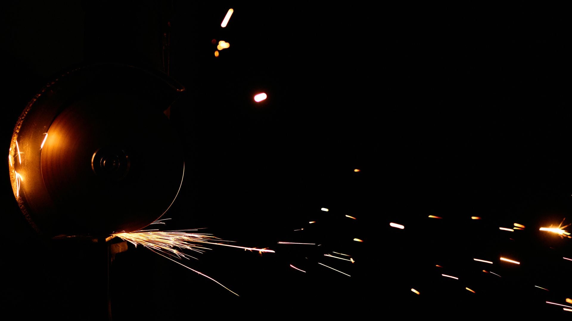 An abrasive cutting wheel throwing a fan of gold sparks across a black workshop background
